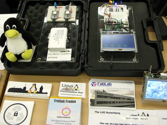 Auf der Hack&Make 2022 auf Messe Nürnberg in der Halle 10. Zu sehen sind auf einem Tisch unsere kleine Hardwareprojekte, welche alle mit freier Software laufen: Die NoteMCUs, Unser GPIO-Board und der Mini-PC. Sowie einige Aufkleber. Ein kleiner Tux darf natürlich auch nicht fehlen.