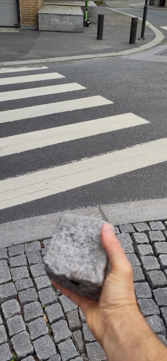 Hånd som holder brostein ved fotgjengerfelt.