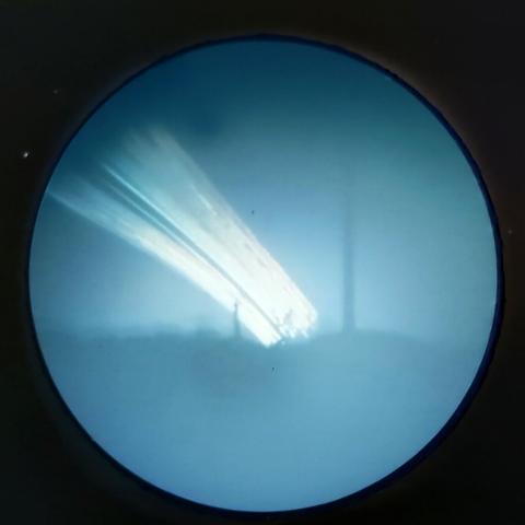 A round solargraph with the sun's arcs showing as white against a blue base. The horizon is just below the centre-line of the image, and the lighthouse is just left of centre. Much taller appearing is the nearby power pole, just to the right of centre. 
The solar arc rise from the horizon in the centre, and arc to the left.