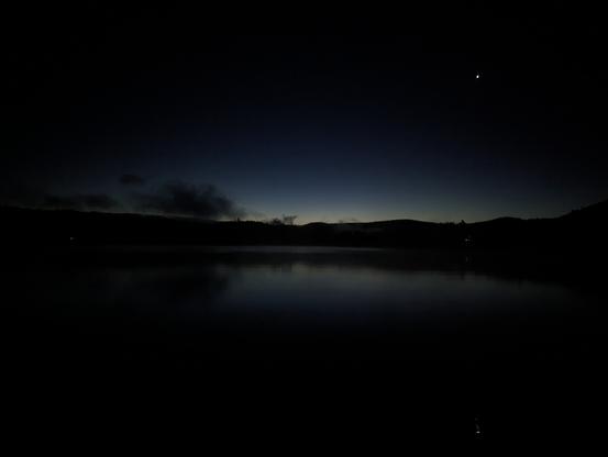 Dark except pale light over mountains, reflected on the water