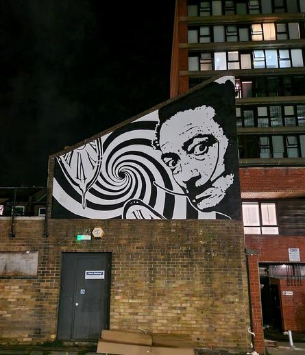 Streetartwall. On the wall of a small brick house has been sprayed / painted black - white mural with the painter Dali. His deliquescent clock and a spiral are arranged next to a Dali with twisted mustache and piercing gaze