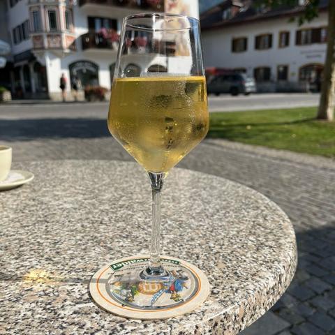 Ein Glas Weißwein in Großaufnahme vor einer oberbayerischen Häuserkulisse.