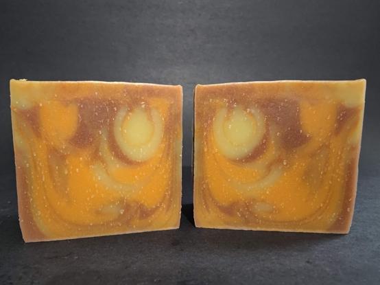 Two bars of cream, brown and orange swirled soap on a dark background
