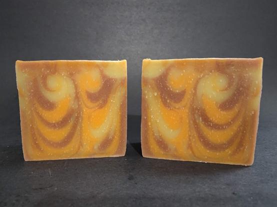 Two bars of cream, brown and orange swirled soap on a dark background