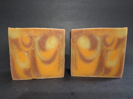 Two bars of cream, brown and orange swirled soap on a dark background