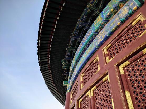 This is the exterior of a large, wooden structure.  Visible is part of the wall of the round building and the roof.  The walls are burnt red with gold accents.  An ornate blue strip circles the building, close to the roof.