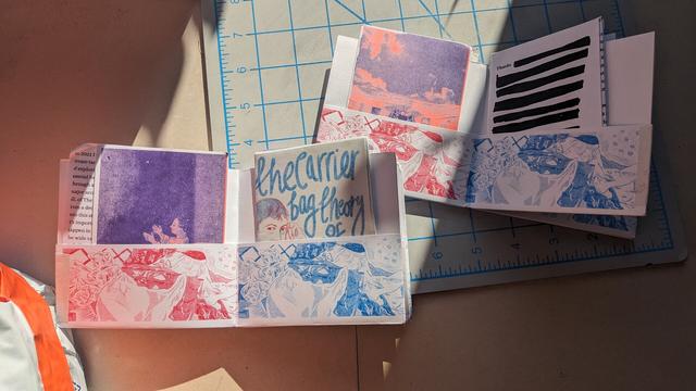 A pair of zines printed in vibrant riso ink, featuring illustrations of Ursula Le Guin, shopping bags, and sunsets. Smaller zines are tucked into the pockets of the larger one