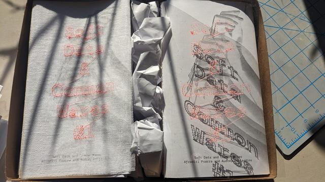The zine Soft Data and Common Wares. The title is stitched onto the cover using a computer controlled embroidery machine, in floro orange thread and on a variety (clear plastic, white mesh) backgrounds