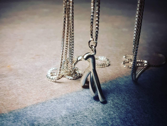 A small silver pendant in the shape of an anatomical clitoris hangs among silver chains.