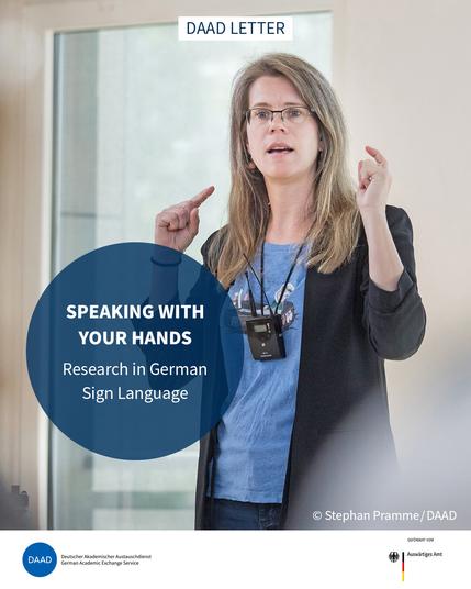 Dr Cornelia Loos, a woman with long blonde hair, is standing in front of a window, signing. A round eye-catcher shows the title: Speaking with your hands. Research in German Sign Language. Image source: Stephan Pramme, DAAD.