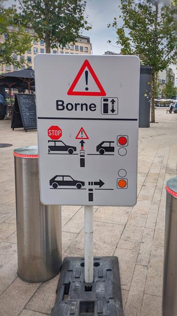 a very complex sign in front of automatic bollards getting out of the ground with 2 raws. the first one tries to make people understand that they have to stop at read light because the bollards will get out of the ground. the second that they can pass if it's orange.