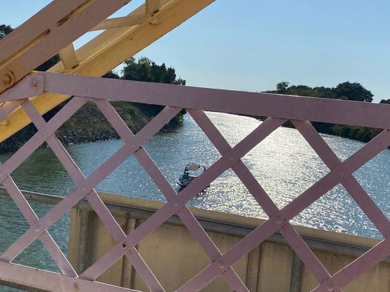 photo taken from passenger seat, looking down the side of the bridge to the river. theres a boat seen between the gaps of the bridges wall.