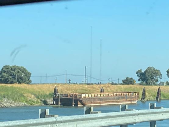 photo of a lonely barge across the Sacramento river. its rust colored sides shows the age and how long its been in service.