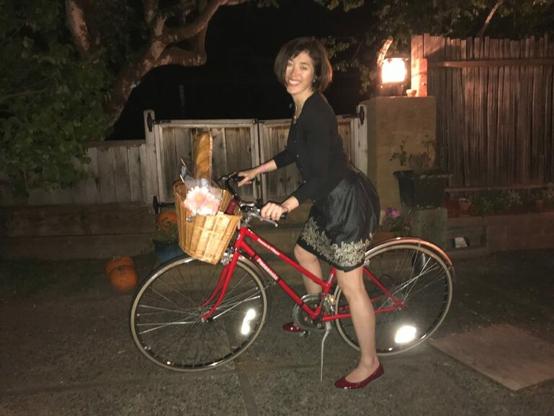 A woman dressed in a dressy black top and black knee-length skirt, and sparkly red shoes, is on her red bicycle at night, preparing to leave her home for a social gathering.  

What we asked her: If she taps the heels of those ruby slippers together three times, will she get home faster? :)