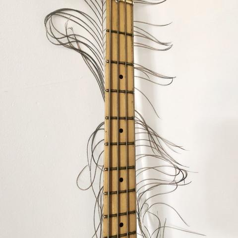The neck of a Fender Precision bass guitar with strands of a peacock feather poking out from behind it.