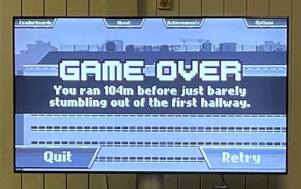 The screen of a TV with words "Game over, you ran 104m before just barely stumbling out of the first hallway," showing the end of a game.