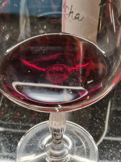 Close up of a wine glass with a little wine in the base. A reflection of light looks like horns coming from the point where the stem joins the bowl of the glass.