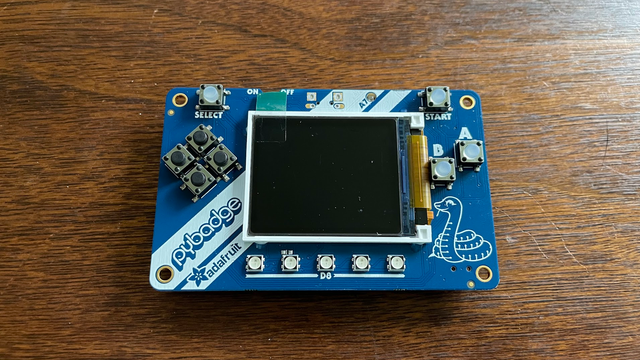 A picture of an Adafruit PyBadge sitting on my desk, waiting patiently for a working Uxn ROM to be uploaded