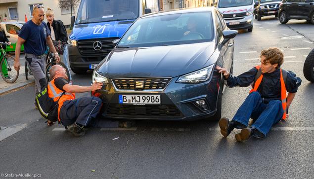 Eine Autofahrerin fährt einen am Boden sitzenden LG-Aktivisten an. Dieser scheint zu schreien oder ihr etwas zuzurufen.