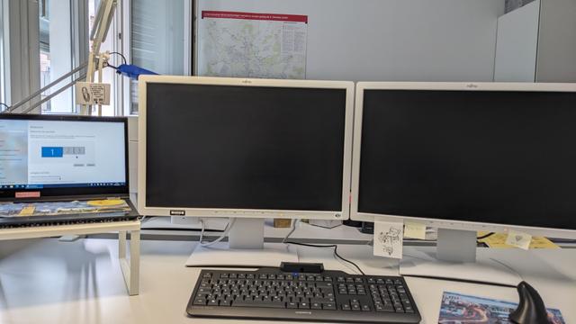im Prinzip 3 Bildschirme nebeneinander: links ein Laptop, in der Mitte ein großer Bildschirm und rechts ein großer Bildschirm. Davor eine Tastatur und eine Maus.