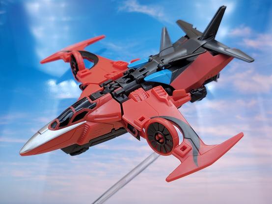 A photo of Transformers Adventure Windblade, in jet mode, in front of a sky backdrop.