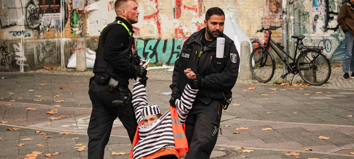Aktivist*in der letzten Generation als Häftling verkleidet wird von der Polizei weggetragen