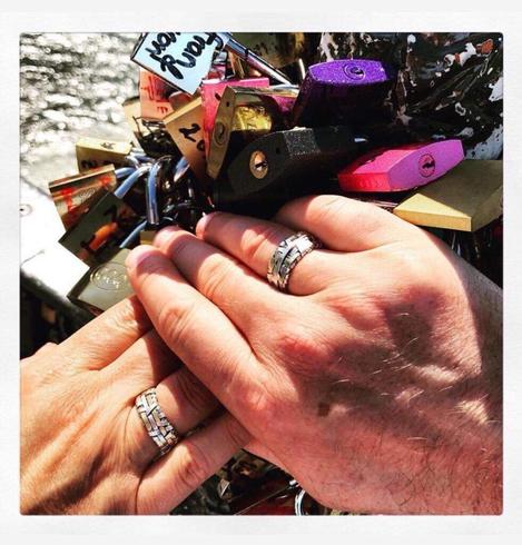 with the backdrop of love lock at a bridge in Paris, two hands holding each other wearing woven rings by gurgel-segrillo