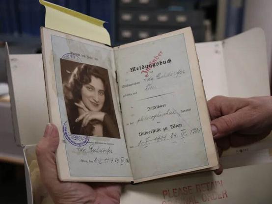 A book is being held and opened to a page with a black and white photo of a woman on it. There are official stamps on the pages.