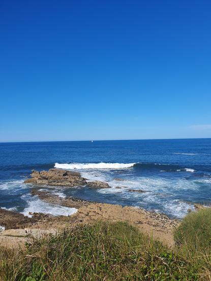 die wellen des atlantik brechen sich an schroffen felsen, darüber ein blauer himmel