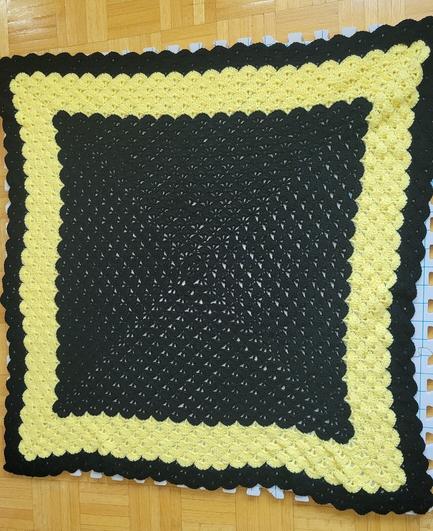 Mostly black, square crochet blanket with a large yellow stripe near the edges.