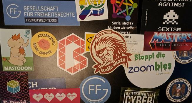 A-cover eines Notebooks. Auf ihn zu sehen sind viele Sticker und in der Mitte ein Kollemate Dicker