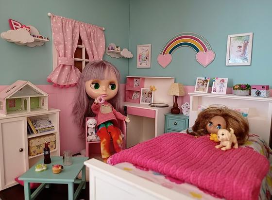 Blythe doll in the chair, holding a doughnut. In bed, next to her a petite Blythe. There are 2 dogs in the scene, which is located in a miniature doll bedroom, with many little details