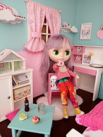 Blythe doll in the chair, holding a doughnut. The doll is in a miniature doll bedroom, with many little details. Sitting with her in the chair, a little dog, hoping to get some crumbs from the delicious doughnut!!
