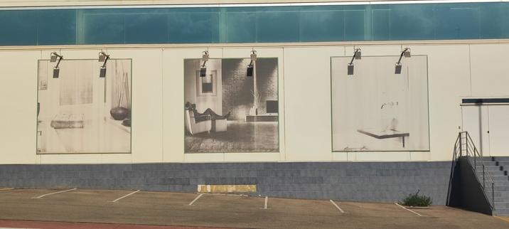 Una imagen de una pared con tres carteles cuadrados. Los focos hacen sombra con pinta de ojos. El contenido de los carteles de los extremos parece completar una boca de la cara.