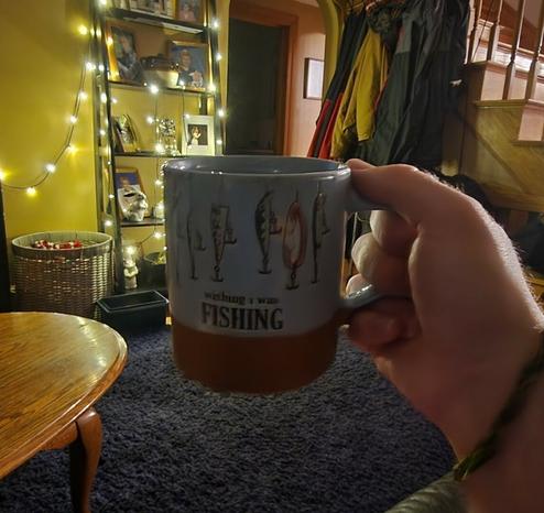 hand holding a mug inside of a room with a string of white lights