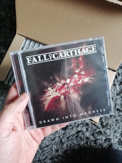 Hand holding a CD: Drawn into madness by Fall Of Carthage
