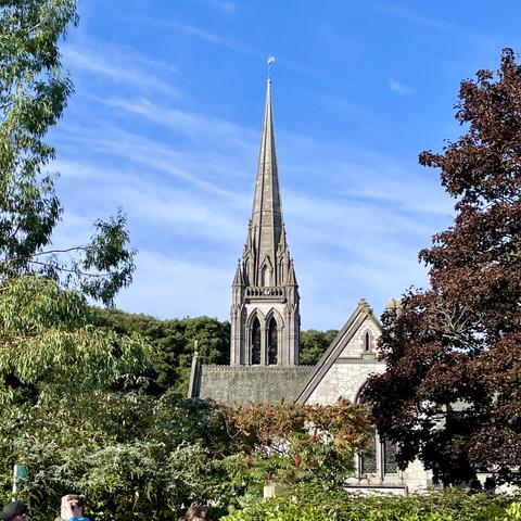 Late 1800s Gothic-style church spire. Trees and blue skies.