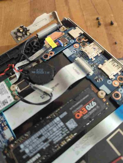 Un ordi portable Clevo N151CU. Le capot du dessous est ôté. On voit quelques composants sur la carte mère, notamment le disque SSD, la carte USB et sa nappe, la pile, la carte wifi je crois, le connecteur d'alimentation 19V. Et surtout, une des deux charnières de l'écran, dont trois vis sont entourées de leur écrou et du plastique cassé qui constitue normalement le socle de fixation de la charnière à la carte mère. Donc la charnière ne tient plus que du côté écran et sa fixation côté carte mère est détruite.