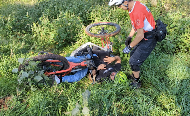 Adaptive mountain bike rider flipped upside down off the trail in a patch of rocks and weeds
