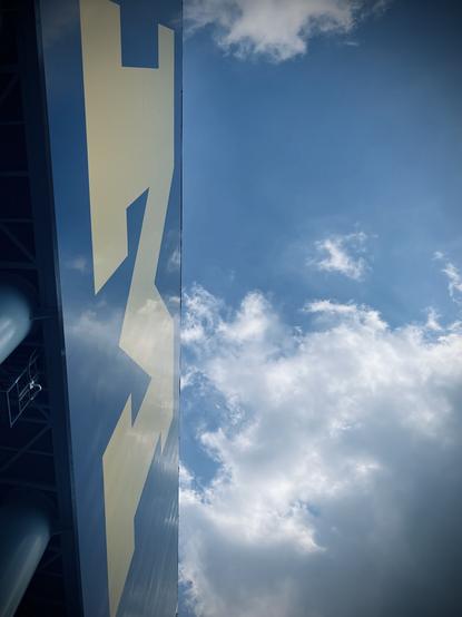 The University of Michigan’s logo outside of the Big House stadium. A shot from below, with clouds in the background.