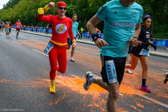 Läufer*innen beim Berlin-Marathon und orangene Pfütze nach Farbattacke der Letzten Generation, Ein Mann läuft im Kostum der Comic-Figur Flash. Straße des 17. Juni, Berlin, 24.09.2023