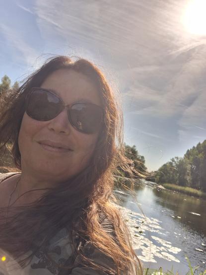 Selfie met op de achtergrond water, bomen en de zon.
