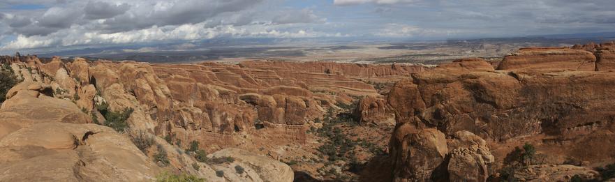 A hand-stitched panorama of the Devil’s playground, lines of vertical red rock formations standing in parallel, with touches of green life scattered throughout while the clouds gather on the horizon.