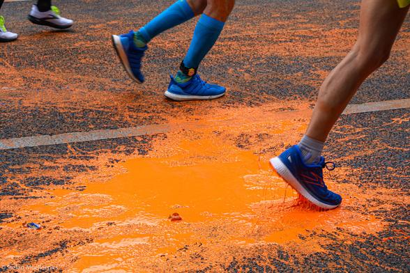 Läufer*innen beim Berlin-Marathon laufen durch orangene Pfütze nach Farbattacke der Letzten Generation. Straße des 17. Juni, Berlin, 24.09.2023