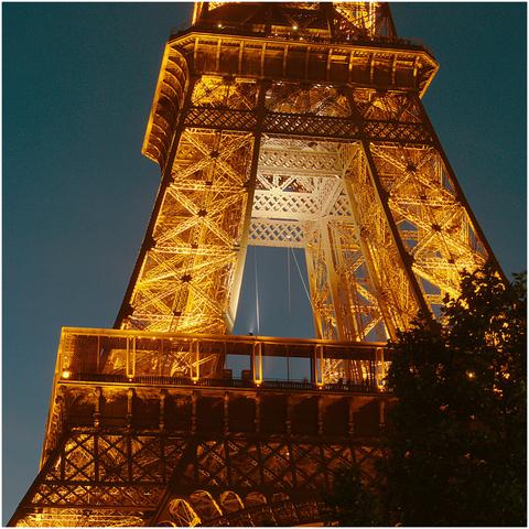 Détail de la tour Eiffel (premier étage), photographiée depuis le sol. Photo de nuit. Le rétro-éclairage du monument la détache du ciel bleu nuit.