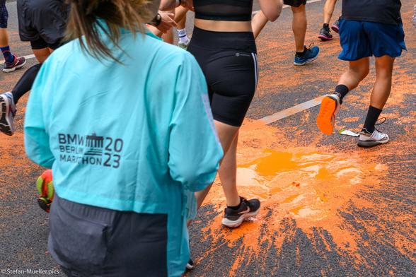 Läufer*innen beim Berlin-Marathon laufen durch orangene Pfütze nach Farbattacke der Letzten Generation. Straße des 17. Juni, Berlin, 24.09.2023