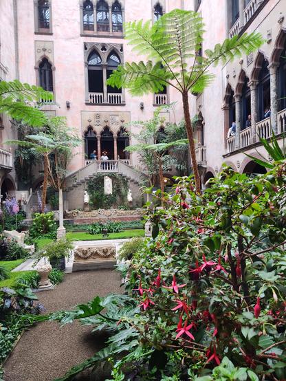 The Italian courtyard of the Isabella Stewart Gardner Museum with fuschia in the foreground,  a central gravel and tike area surrounded by 4 stories of interior walls.
