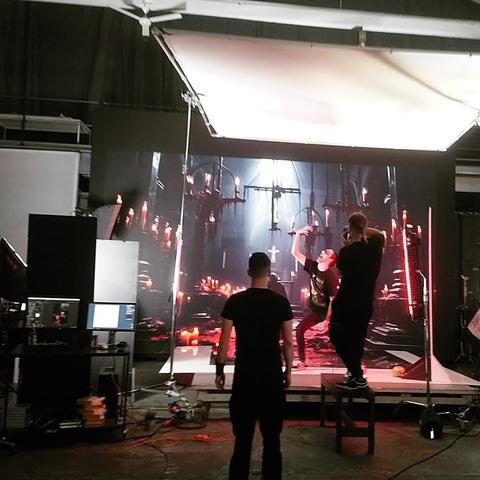 Behind the scenes von einem Photoshooting, inklusive Corpse Paint und einer Videoleinwand auf der eine dämonisch verunstaltete Kirche zu sehen ist.