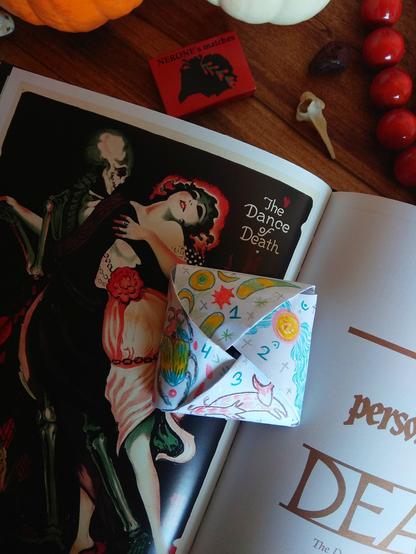 The other side of the letter. There are a bug, two bulls, some horns, a moon and some angel-kind-of creature. 
On the background: a book with a spooky art (woman dancing with a skeleton), some pumpkins, a matchbox (red), a bone, red jewelry.