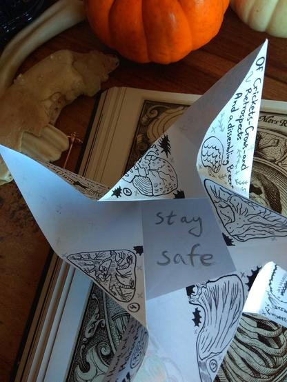 The very inside part of the letter. It is written here: 'stay safe' (silver). 
On the background: a book with a spooky art (skeleton), some pumpkins, a matchbox (red), a bone and a piece of a jaw, red jewelry.